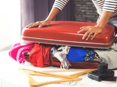 Travel and vacation concept, happiness young woman packing a lot of her clothes and stuff into suitcase on bed prepare for travel and journey trip in holiday.